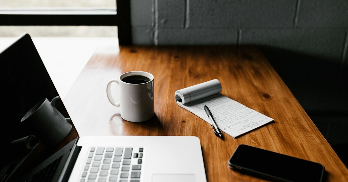 Laptop and notebook for custom research paper writing on a wooden desk